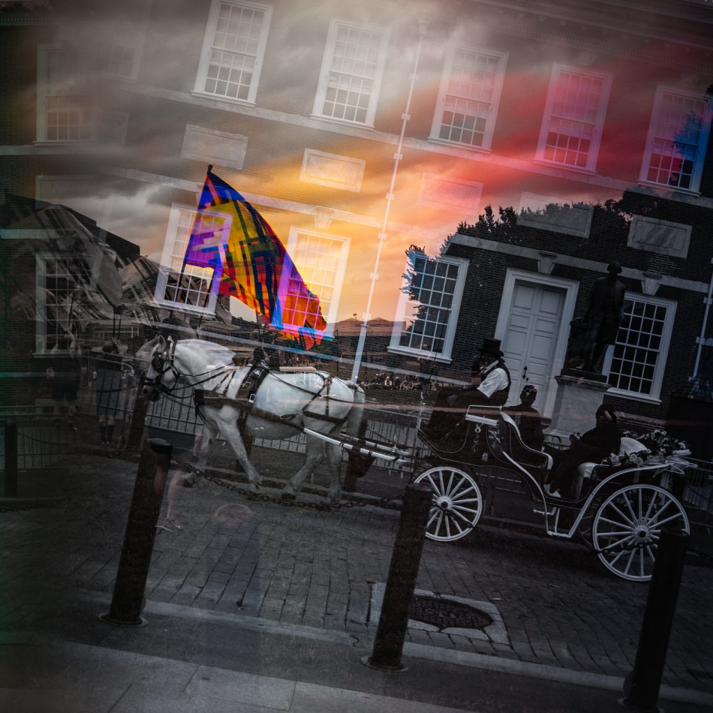 Selectively color restricted photo of gay pride flag twirling team practicing set over Philadelphia's independence hall with horse drawn carriage passing through. 